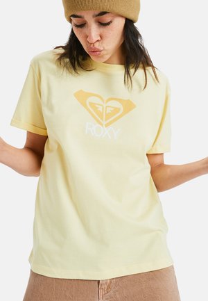 T-shirt en coton jaune clair avec un design de cœur en orange, portant "ROXY" imprimé en dessous. Manches courtes et coupe décontractée.