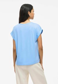 Top azul claro de manga corta con un ajuste holgado, cuello redondo y puños enrollados. La tela tiene una textura suave, adecuada para uso casual.
