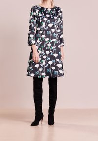 Abito a fantasia floreale in tessuto scuro, con maniche lunghe e scollo rotondo, abbinato a stivali alti in suede neri.