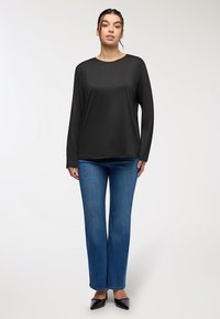 Maglietta nera a maniche lunghe con scollatura rotonda, abbinata a jeans a zampa d'elefante blu medio e scarpe nere a punta, su uno sfondo chiaro.