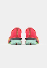 Nike sneakers met een felroze mesh bovenwerk, gele accenten en een zwarte tussenzool. De zool is mintgroen met een gestructureerd oppervlak.