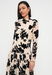 Φλοράλ φόρεμα με γυμνό βάση και μαύρα λουλουδάτα μοτίβα, μακριά μανίκια, ψηλός λαιμός και πτυχωτή φούστα. Λείο ύφασμα.