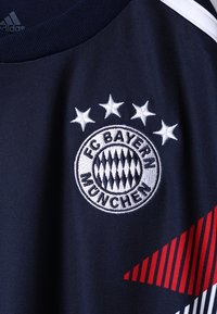 Navy sports jersey features a circular embroidered FC Bayern München logo with four stars above; red diagonal stripes on the side.