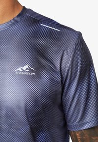 Maglietta atletica a maniche corte di colore blu scuro con un motivo testurizzato a punti. Presenta dettagli riflettenti e un logo bianco.