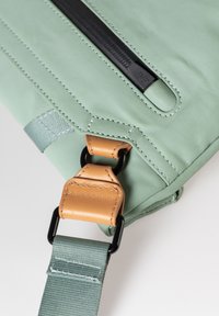Borsa a spalla verde con esterno testurizzato, zip nera, dettagli in pelle beige e una robusta tracolla in tessuto con accessori neri.