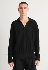 Schwarzer Strickpullover mit strukturiertem Gewebe, ausgestattet mit einem breiten gerippten Kragen und langen Ärmeln. Enthält ein kleines Logotag am Saum.