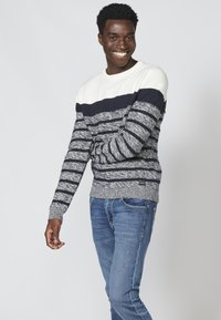 Gebreide trui in navy en witte strepen met een textuurafwerking. Heeft een ronde halslijn en ribgebreide manchetten. Gepaard met blauwe spijkerbroek.