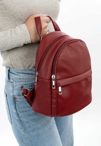 Zaino in pelle rossa con una forma arrotondata, finitura testurizzata e due cerniere. Presenta una maniglia superiore e una tracolla regolabile.
