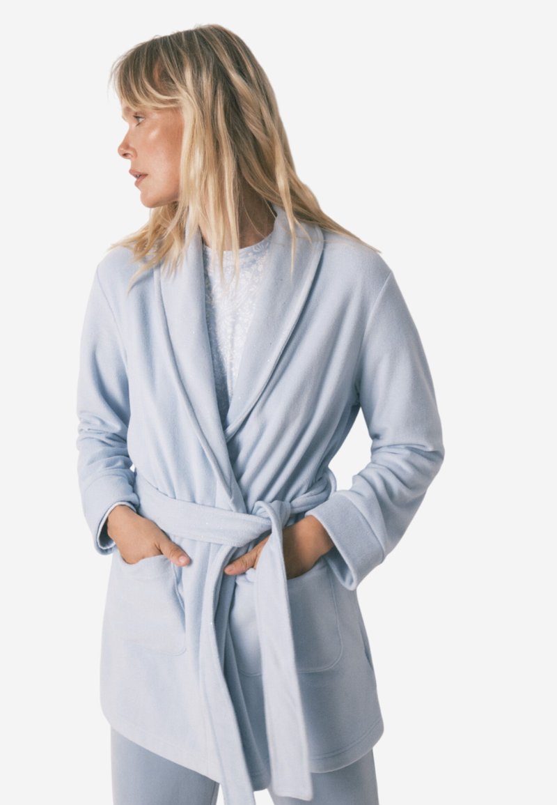 Robe bleu clair en tissu doux et texturé, avec une taille ceinturée, un col châle et deux poches avant.