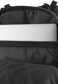 Čierny batoh s polstrovanou priehradkou, ktorý má zipsové uzatváranie a sieťovinu. Obsahuje strieborný laptop, ktorý je viditeľný v hlavnej kapse.