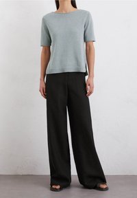 Lyseblå strikket sweater med korte ærmer og afslappet pasform, parret med sorte vidde bukser og flade sorte sandaler. Minimalistisk design.