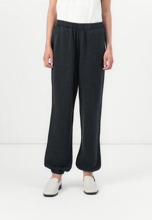 Svart, løse joggebukser med elastisk midje og ribbestrikkede legger. Materialet har en glatt tekstur. Brukes med hvite slip-on sko.