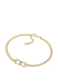 Bracelet en chaîne dorée avec un symbole de l'infini, avec de petites pierres transparentes en accent. Le design comprend deux chaînes entrelacées.