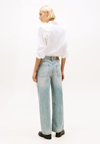 Light blue high-waisted jeans with wide legs, featuring back pockets and subtle fading, paired with a long-sleeve white shirt.