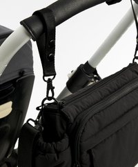 Zwarte stoffen tas met ritsen en meerdere vakken, bevestigd aan een kinderwagenhandvat met drukknoopclips. Afgeronde strap voor grip.