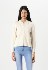Cardigan lavorato a maglia di un beige chiaro con zip frontale, colletto a punta e maniche lunghe. Texture liscia, design aderente e orlo corto.