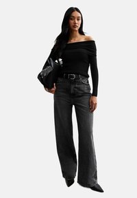 Schwarzes schulterfreies Oberteil, hoch taillierte schwarze Denim Weitbein-Hose, spitze schwarze Absätze und eine schwarze Handtasche mit silbernen Hardware-Akzenten.