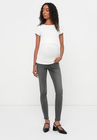 White short-sleeve top with a curved hem and a maternity fit, paired with slim-fit gray jeans and black pointed-toe heels with ankle straps.