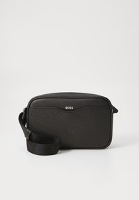 Black crossbody bag with textured material, rectangular shape, zip closure, and an adjustable strap. Features a subtle logo on the front.