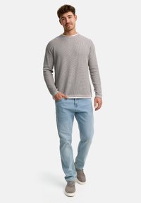 Camisa de manga larga gris claro con un patrón texturizado, combinada con jeans de mezclilla azul claro y zapatillas grises. Diseño simple y de corte relajado.