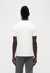 Λευκό βαμβακερό T-shirt με κοντά μανίκια, στρογγυλή λαιμόκοψη και ελαφρώς άνετη εφαρμογή, σε συνδυασμό με γκρι παντελόνια. Λείο ύφασμα.