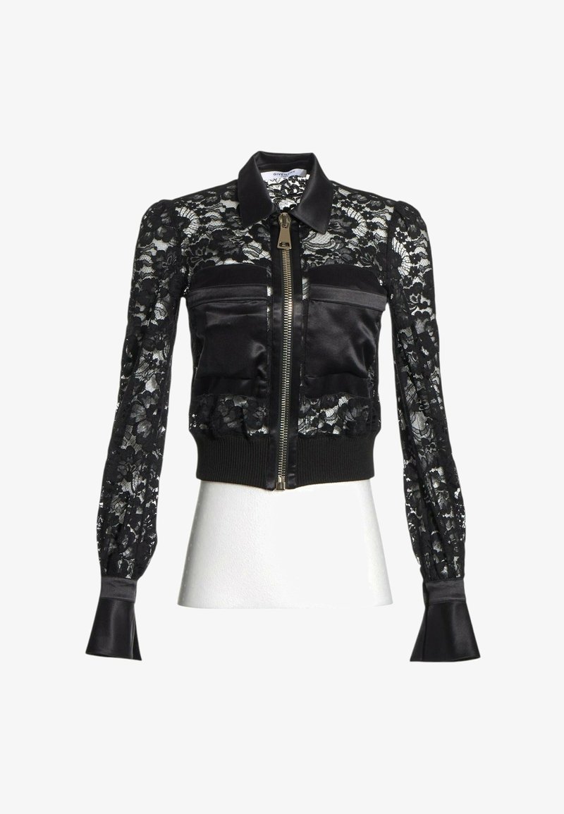 Veste en dentelle noire à manches longues, col en satin, fermeture éclair à l'avant, deux poches poitrine en satin et ourlet côtelé, présentée sur un buste de mannequin blanc.