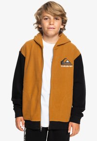 Bruine en zwarte fleece zip-up hoodie met een voorzak, een capuchon en een Quiksilver-logo op de borst. Lange mouwen, zachte textuur.
