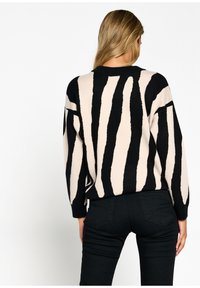 Suéter de punto en beige con atrevidos rayas negras. Presenta un cuello redondo y un corte relajado. La tela texturizada resalta el diseño.