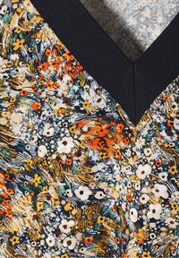 Floral patterned fabric featuring a mix of orange, yellow, and white flowers on a dark background with a V-neckline and textured finish.