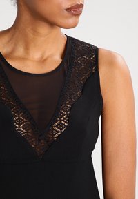 Robe noire avec une insertion en dentelle transparente dans un design à col en V. Le tissu est lisse, avec un détail en dentelle texturée le long du décolleté.