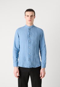 Lichtblauw overhemd met lange mouwen in een gestructureerde stof, met een staande kraag en knoopsluiting aan de voorkant. Zwarte broek maakt de outfit compleet.