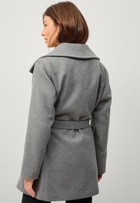 Grijze wollen jas met een brede kraag, een ceintuurlijn en lange mouwen. Heeft een gestructureerde stof met een gladde afwerking en geen zichtbare hardware.