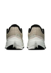 Des chaussures de sport beige et noires avec une tige lisse, une semelle rembourrée et un design de talon unique avec des accents blancs contrastants et un branding.