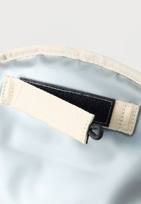 Κοντινό πλάνο μπεζ υφασμάτινου λουριού με αυτοκόλλητο Velcro και μαύρη θηλιά σε ανοιχτό γκρι φόντο.