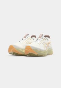 White athletic shoes with a mesh upper, gray accents, orange and yellow sole, and decorative lacing. Features a rounded toe and cushioned design.
