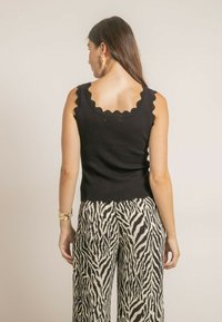 Top sans manches noir avec un col échancré, porté avec un pantalon à jambes larges à rayures zébrées noires et blanches audacieuses.