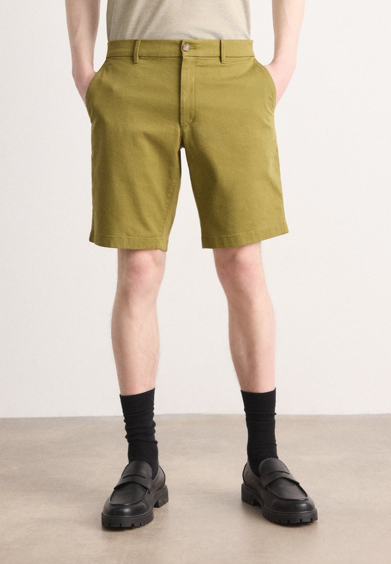 Olivengrønne bomullsshorts med sidelommer, knappelukking og rett passform, paret med svarte sokker og loafers.