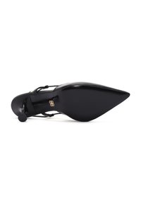 Scarpa nera con tacco alto e punta affusolata, tomaia in pelle liscia, sottile cinturino alla caviglia e un piccolo accento dorato vicino al tacco.