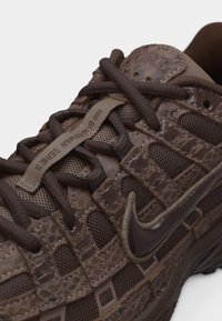 Καφέ αθλητικό παπούτσι Nike με υφασμάτινη επιφάνεια και σχεδιασμό ψεύτικου φίδιου δέρματος, σκούρα καφέ κορδόνια και ορατό λογότυπο Nike στο πλάι.