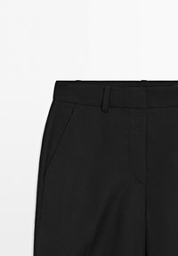 Pantaloni neri con passanti per cintura e tasche laterali, mostrati dalla vita fino a metà coscia su sfondo bianco.