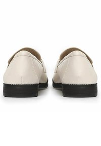 Zapatos de cuero beige con una textura suave, suelas de goma negra y un tacón bajo. El diseño presenta una forma limpia y minimalista con un ribete cosido.