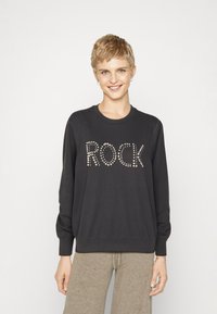 Čierna mikina s nápisom "ROCK" v kovovom študovanom dizajne, s dlhými rukávmi a voľným strihom.