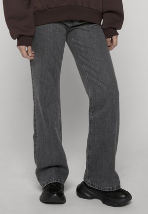 Person iført falmede sorte jeans med lige ben, sorte chunky sneakers og en mørkebrun oversized sweatshirt.