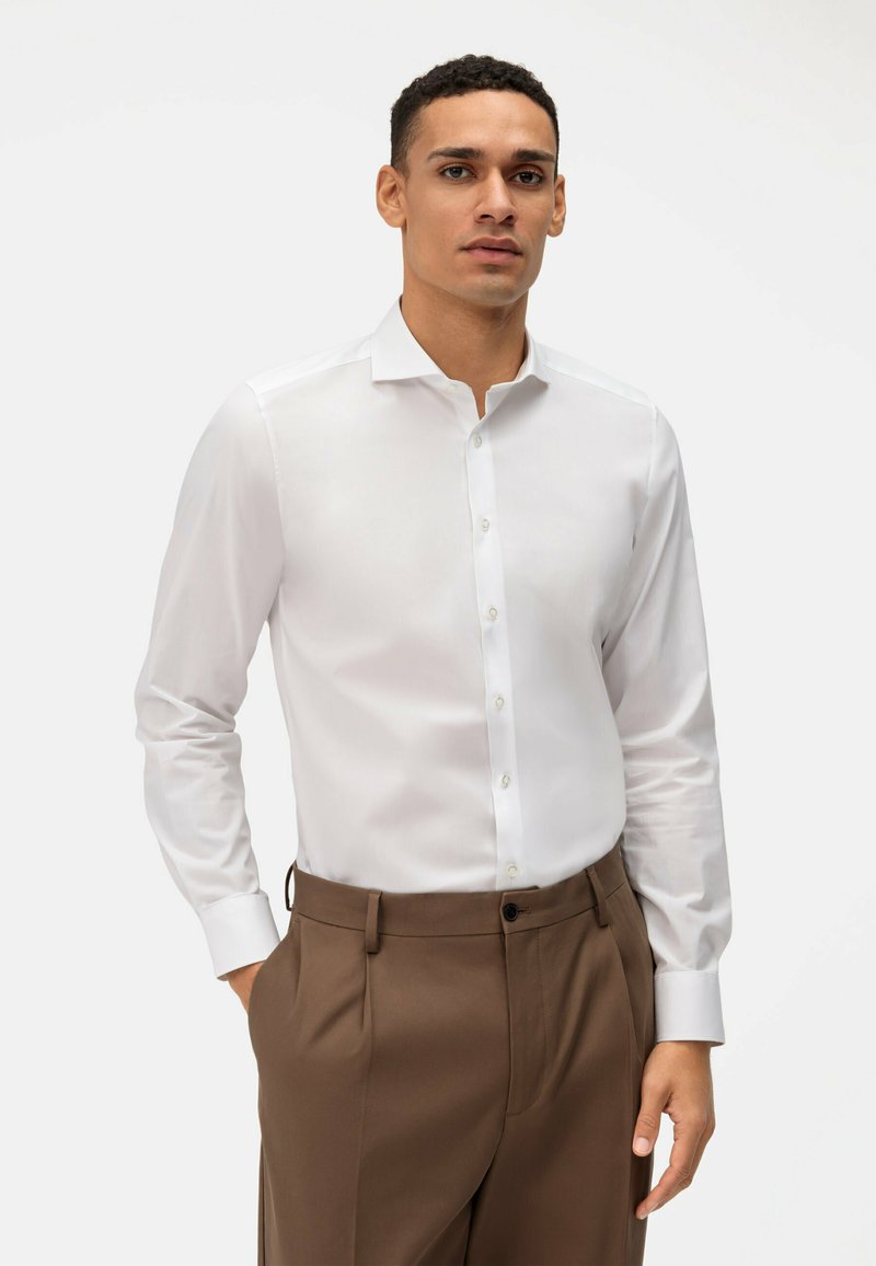Witte blouse met lange mouwen, een puntkraag, knoopsluiting en een gladde textuur, gecombineerd met een bruine broek met een geplooide voorkant.