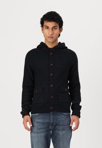 Hoodie tricotat de un bleu închis, cu nasturi pe toată lungimea din față, două buzunare frontale și manșete tricotate. Se remarcă prin nasturi maro și un material texturat.