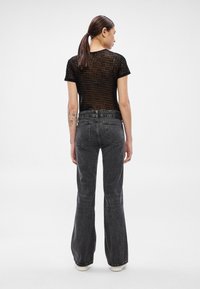 Čierne, priehľadné pruhované tričko s krátkymi rukávmi v kombinácii s vysokým pásom, rozšírenými tmavošedými džínsami. Na spodnej časti viditeľné biele tenisky.