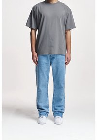 Camiseta de algodón gris de manga corta, combinada con jeans de mezclilla azul claro. Zapatillas blancas completan el atuendo, que tiene un ajuste casual.
