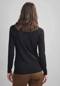 Pull noir à manches longues en tissu doux, avec une coupe ajustée et un col arrondi, bordé de côtes et à la texture lisse.