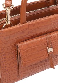 Sac en cuir marron à motif crocodile avec des sections lisses et texturées, comportant une poche avant et des accents en métal doré.