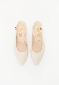 Beige slingback-kengät, joissa on terävä kärki, sileä nahkapinta ja pieni metallikoriste kannan lähellä. Sisäosa vuorattu pehmeällä materiaalilla.